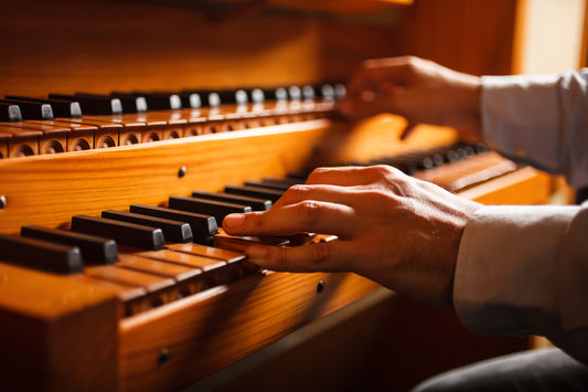 Close-up of an organist's hands playing the warm wooden manuals of a pipe organ in soft golden light