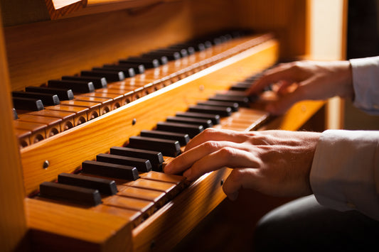 Close-up of an organist's hands playing the warm wooden manuals of a pipe organ in soft light