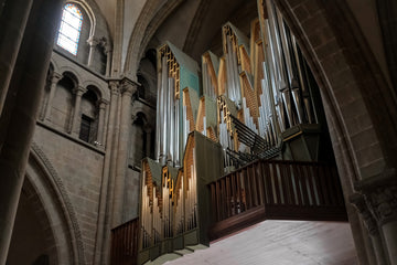 A pipe organ with tall golden pipes set among stone arches in a cathedral, lit by soft warm light