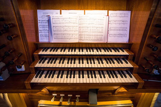 Three-manual wooden pipe organ console with hymnbook and sheet music on the music desk, flanked by drawknobs