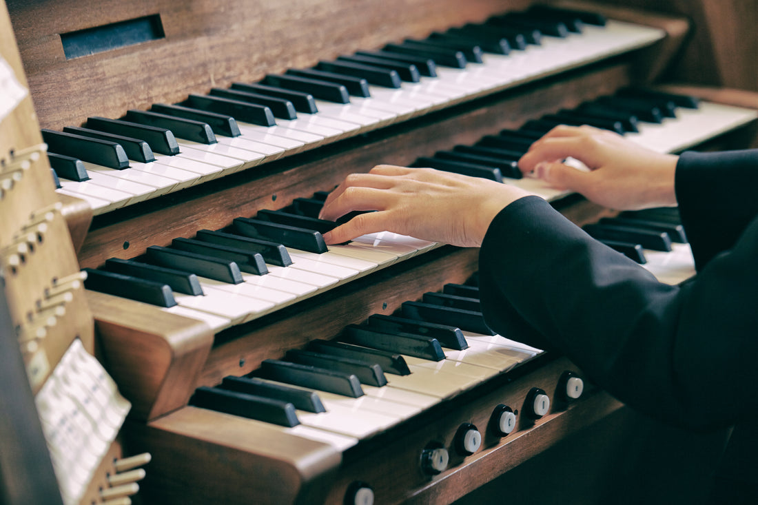 An organist's hands playing the stacked wooden keyboards of a church pipe organ