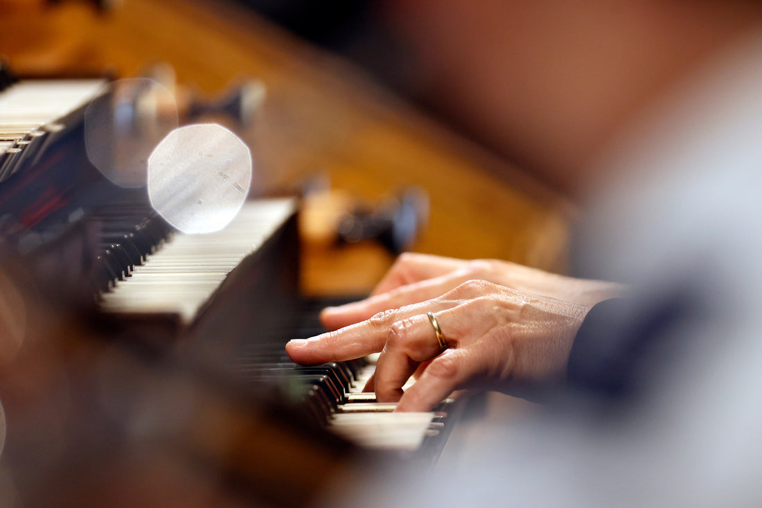 An organist's hand pressing the keys of a church organ console, stacked manuals softly blurred in warm light
